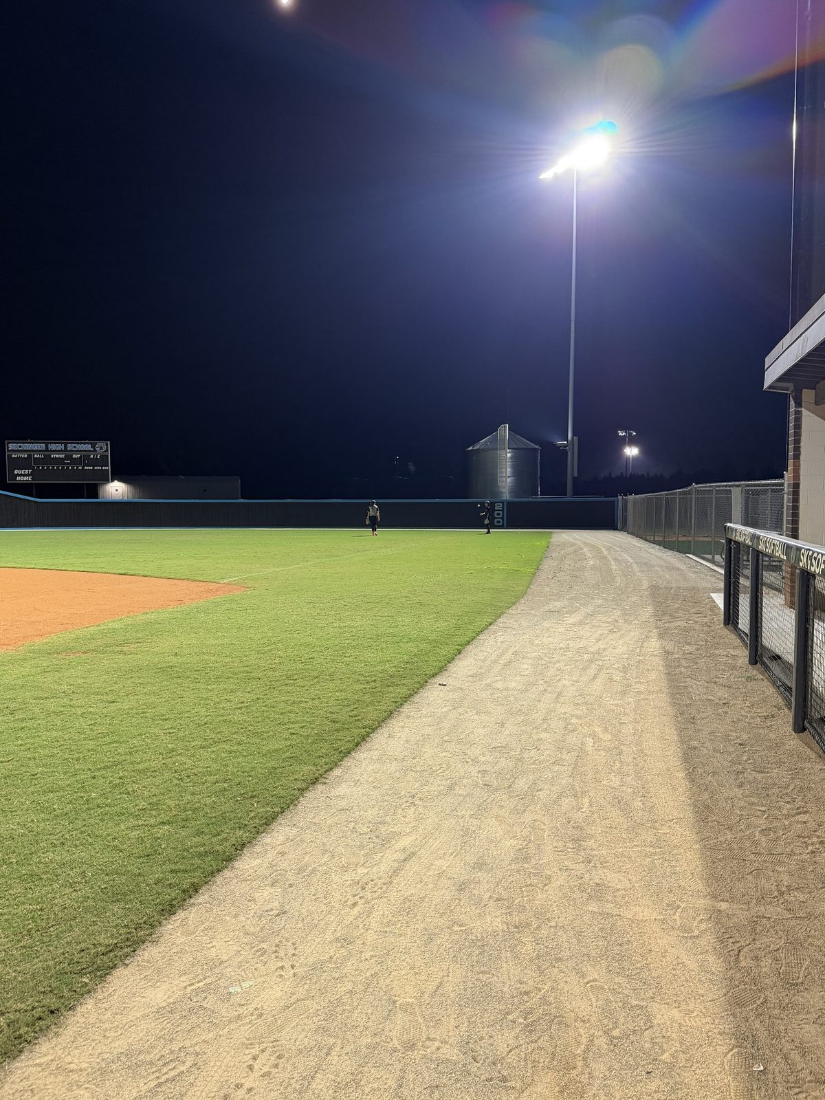 Two ORIGIN athletes in right field at Seckinger High School under the lights, seen down the right-field line.